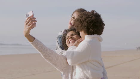 happy american mother and two children taking selfie and making funny faces at camera while spending time at seashore