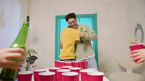 multiethnic young friends playing beer pong at home. caucasian boy throwing the ball, scoring and celebrating with his teammate.