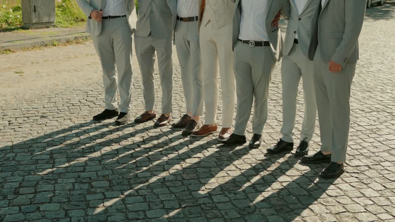 group of friends in identical suits stand together, their shadows cast on the cobblestone street as they embrace