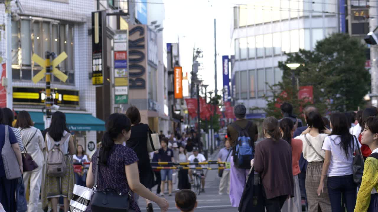 Shot of busy train crossing in Jiyugaoka with a train passing by then the gates opening up for pedestrians to cross.