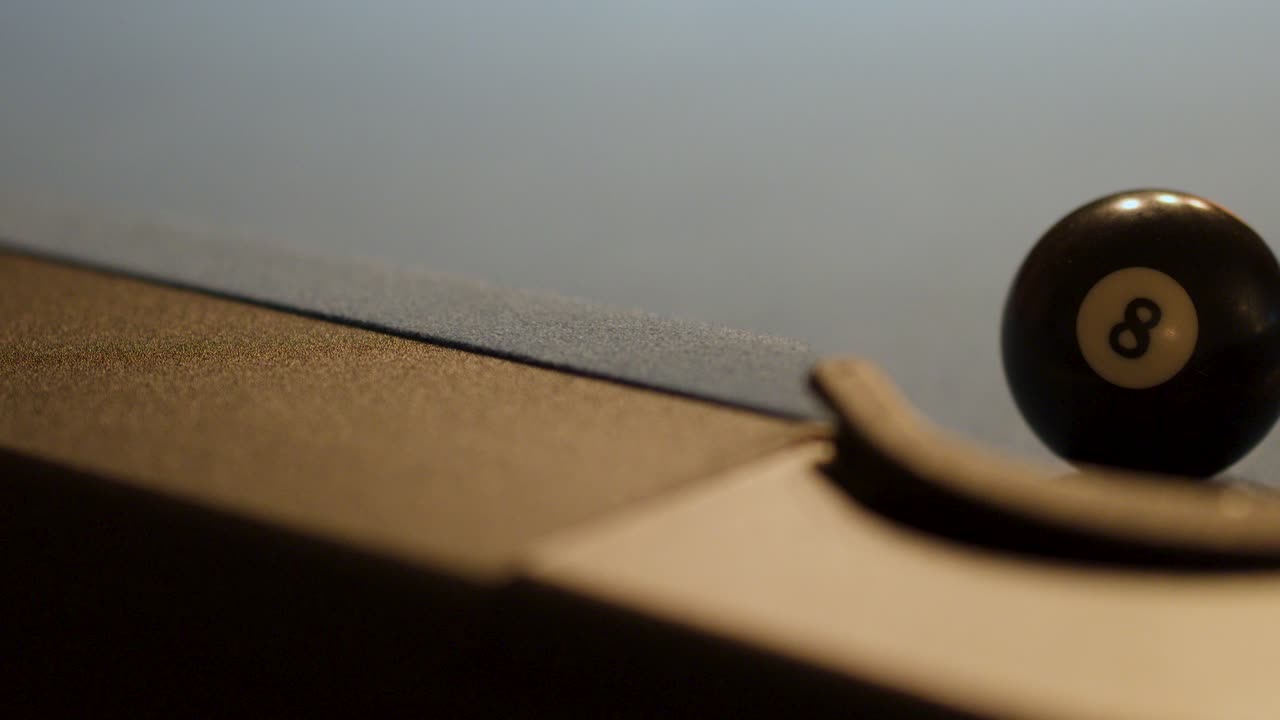 Eight ball is struck, rolls, and drops into corner pocket on dimly lit billiard table