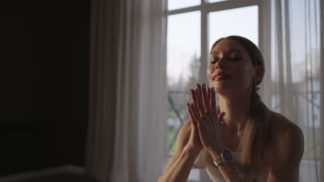 close-up yoga training in the hall with large windows and sunlight passing through the frame. a woman in white sportswear trains in the gym on a mat