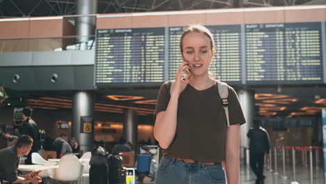 una mujer joven con una mochila está en el aeropuerto y espera su salida retrasada en el aeroporto. llame a la aerolínea debido a retrasos en los vuelos