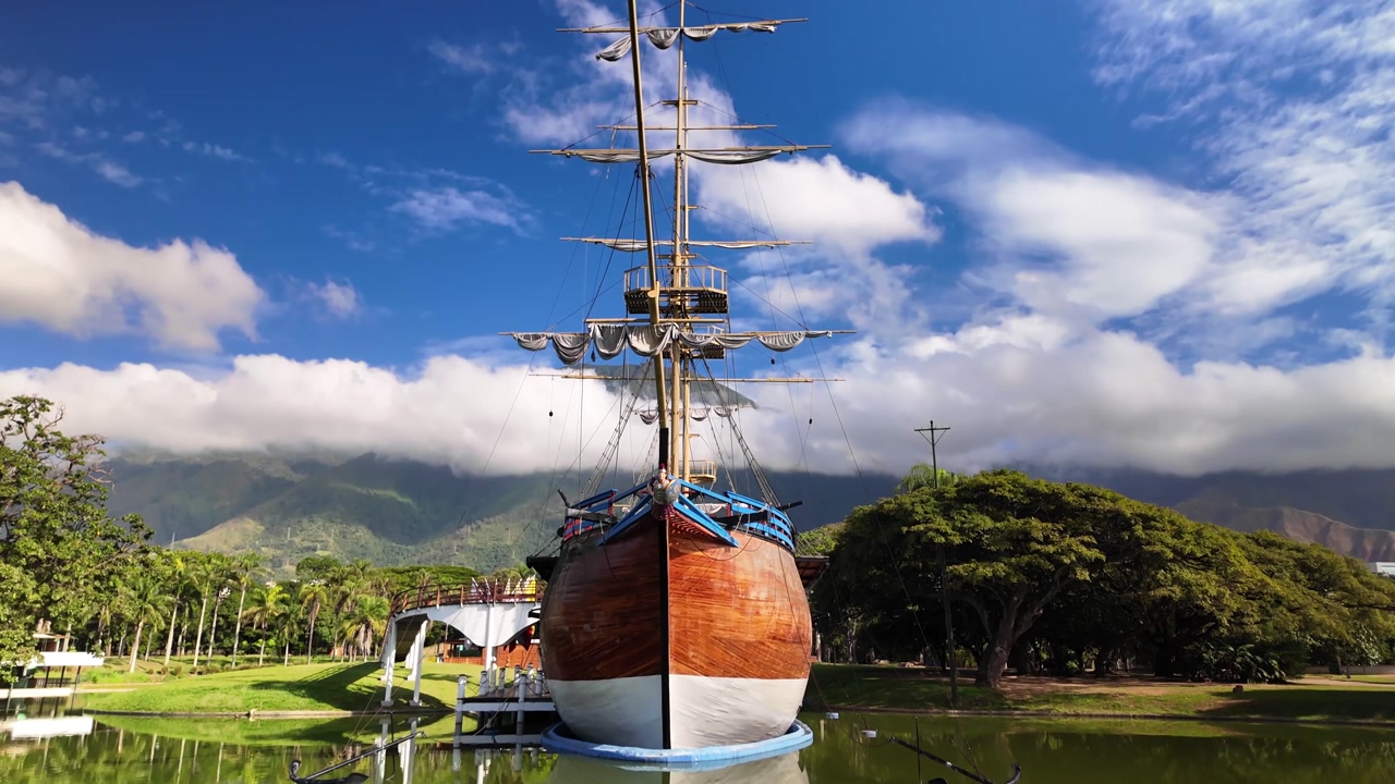 Low angle camera movement over green grass tilting up to show the historic ship inside a sunny public park