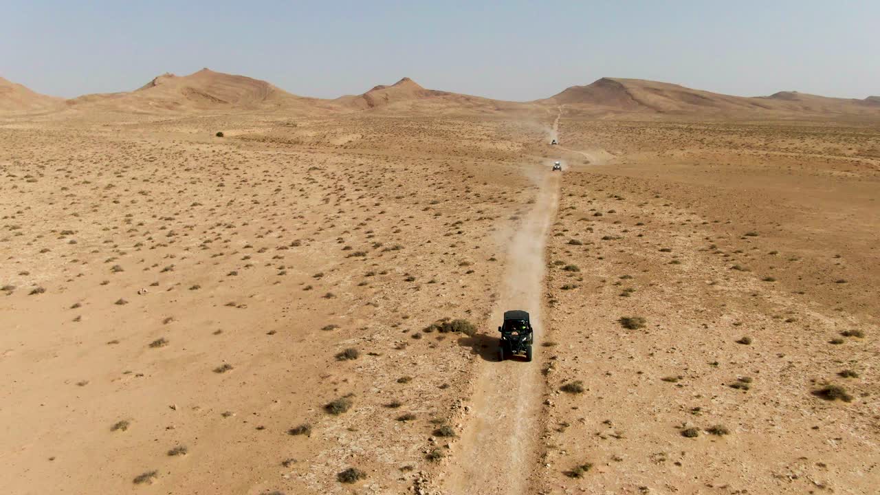 Filmato aereo realizzato con drone che mostra un singolo fuoristrada che si muove lungo una pista polverosa attraverso un vasto paesaggio arido con lontane colline rocciose che enfatizzano l'isolamento, la scala e l'esplorazione