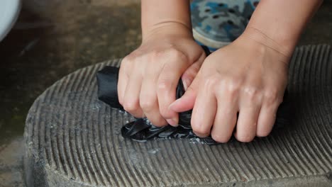 mujer arranca una camiseta, hembra elimina el agua de la ropa lavada exprimiendo líquido en una vieja tabla de lavado de piedra con costillas - las manos de la mujer en primer plano