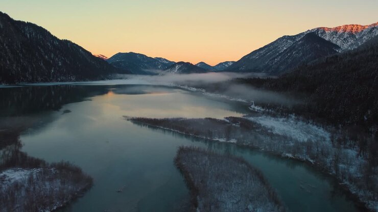 Panoramica valle fluviale di montagna con acqua fresca nelle Alpi bavaresi e austriache, presso Sylvensteinspeicher, al tramonto soleggiato, con il letto del fiume innevato che costeggia alberi, bosco e montagne.