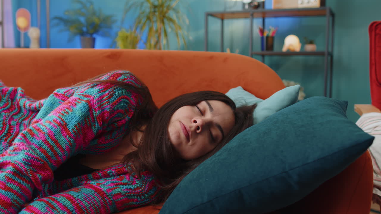 Tired young woman lying down on comfortable couch taking a rest daytime nap relaxing falling asleep