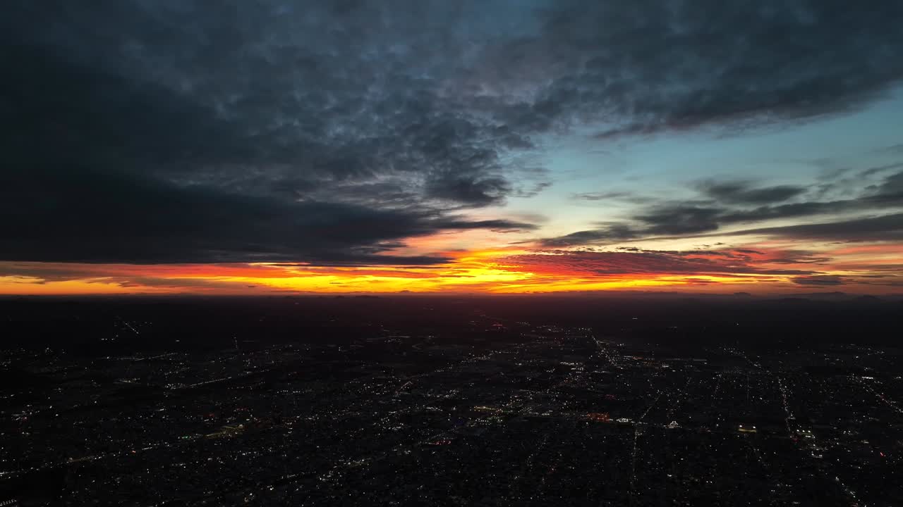 Pimeässä auringonlaskussa drooni laskeutuu, samalla kun kaupungin valot syttyvät värikkäällä ja salaperäisellä taivaalla.