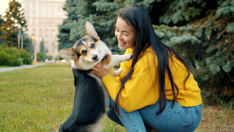 woman kissing her happy corgi dog in a park