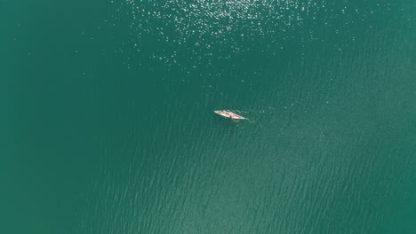 Aerial-top-down,-kayaker-paddling-on-a-blue-turquoise-lake-during-summer