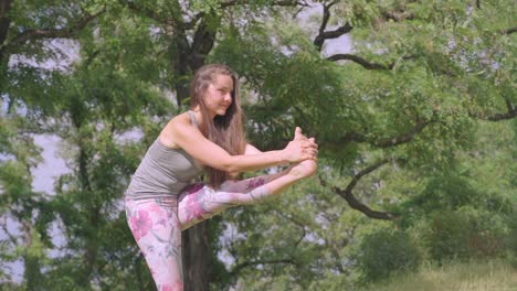 vista lateral de una mujer joven, realizando una pose de yoga de pie a la rodilla al aire libre