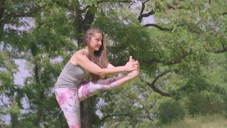 side view of young woman, performing standing head to knee yoga pose outdoors