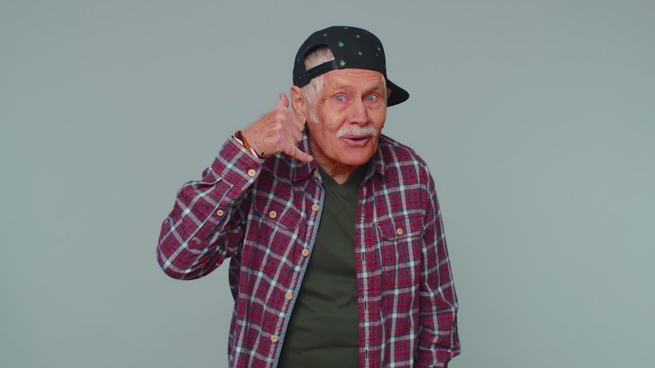 hombre mayor alegre en camisa mirando a la cámara haciendo gesto de teléfono como dice hola me llamas