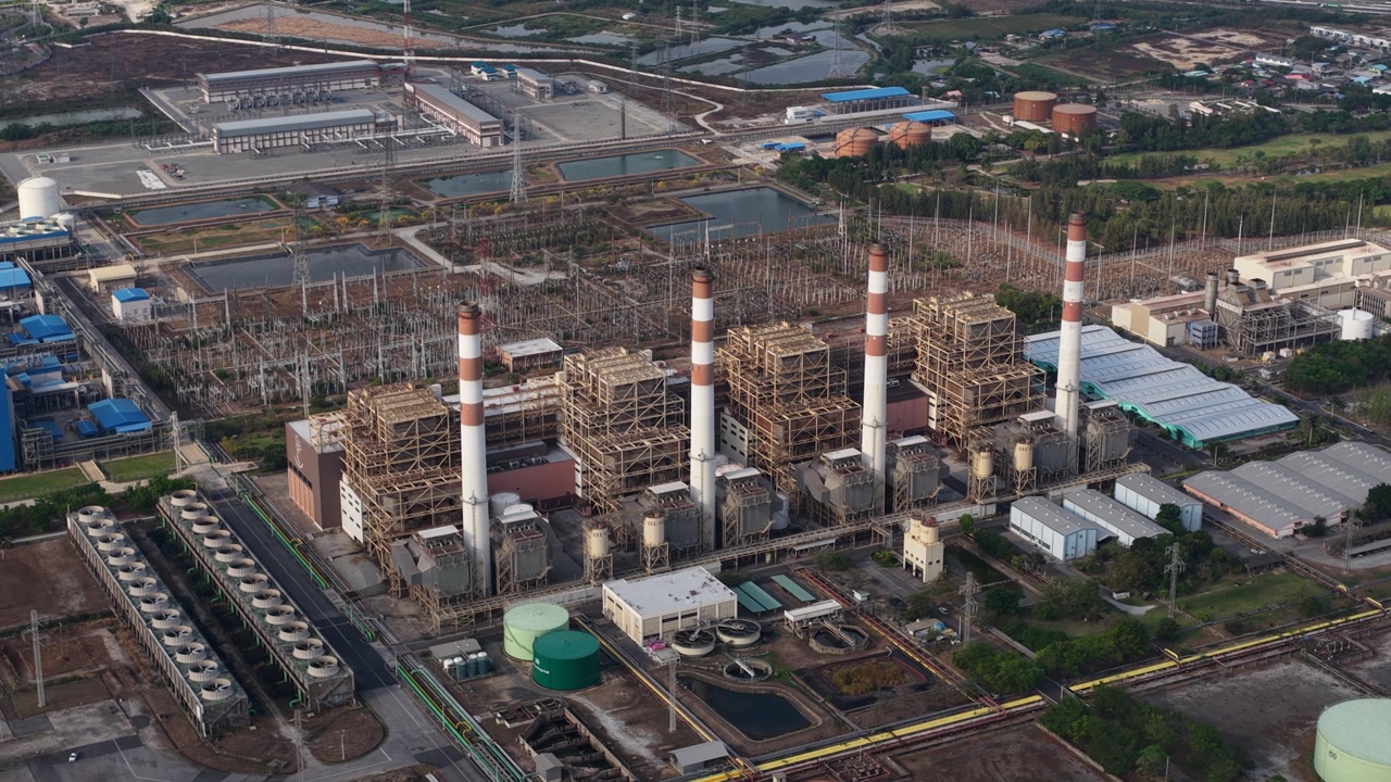 Aerial drone footage capturing the vast industrial landscape of a coal fired power plant, showcasing its towering smokestacks, boilers, cooling towers, and extensive electrical grid infrastructure