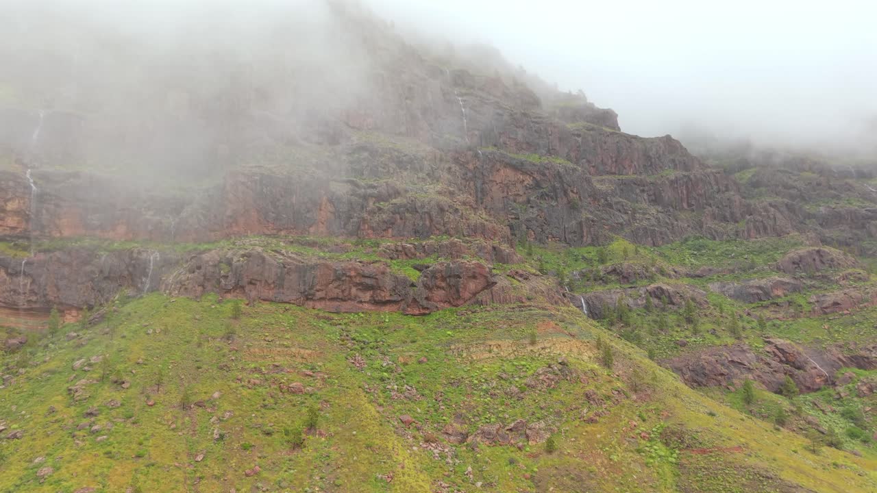 Gran Canaria, Mogan'daki Los Azulejos de Veneguera dağında, fırtına sonrası hareketli sis eşliğinde aşağı akan şelaleler.