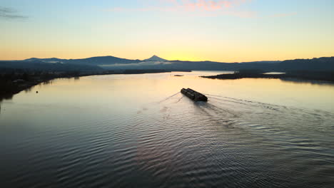 drone panning to the left, watching over a large ship laying in the middle of a big lake during sunrise