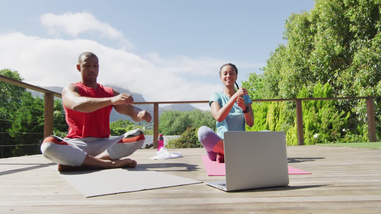 feliz pareja biracial en la terraza haciendo ejercicio, estirándose con lecciones en línea