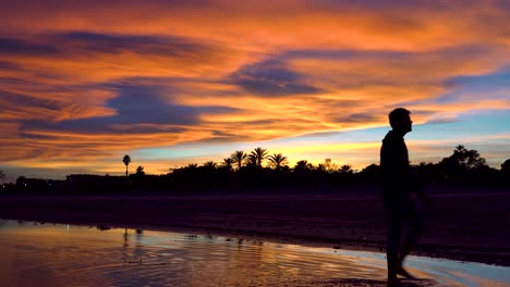 person passing from right to left over the water watching the amazing sunset on a beautiful tropical beach, clouds and amazing colors, amazed