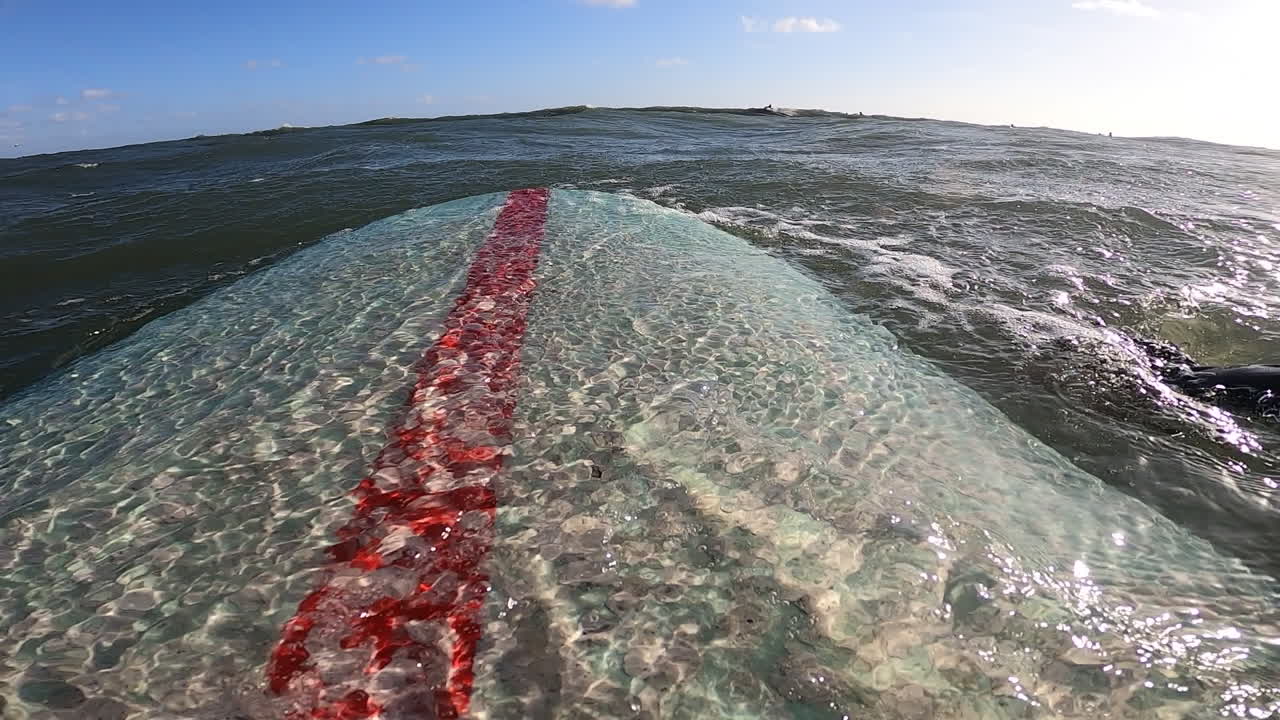 pov, серфер гребет пенопластовой доской для серфинга над океанской волной в летний день с голубым небом