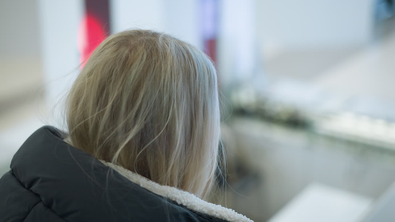 쇼핑몰에서 움직이는 에스컬레이터에서 그녀의 오른쪽을 바라보는 경력 여성의 클로즈업, 흐릿한 배경에서 박이는 빛은 이 도시 장면에 현대적인 터치를 추가합니다.