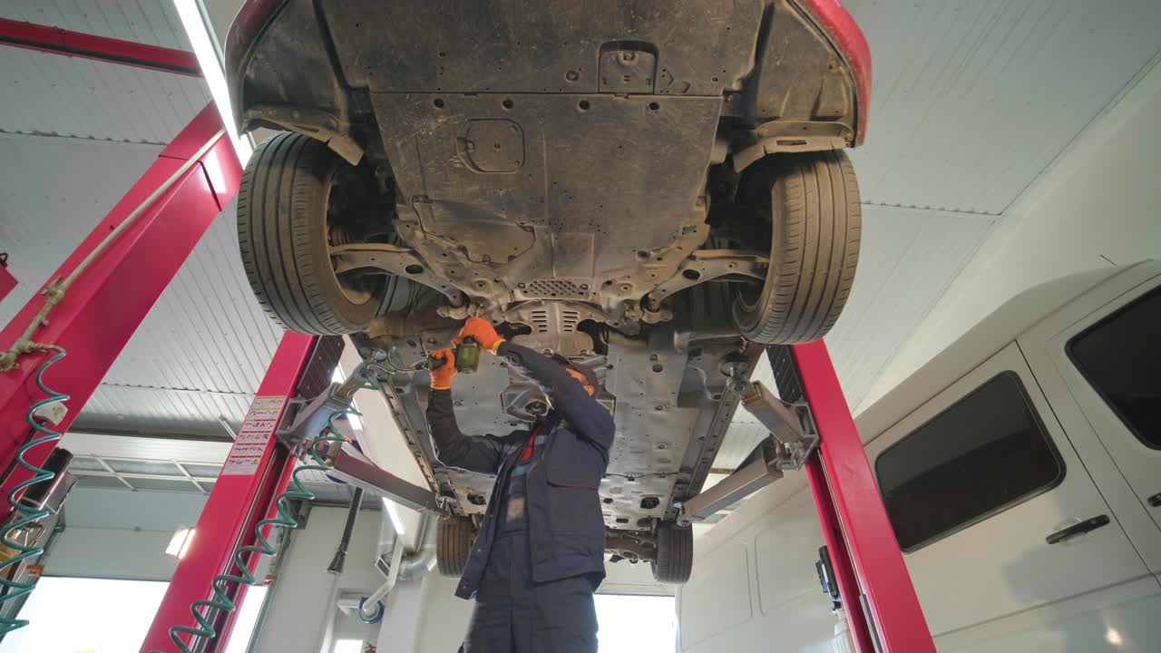 Young professional mechanic man working under lifted modern car in auto repair service. Car service, repair maintenance.
