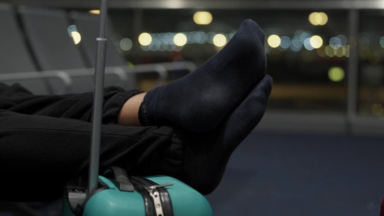 Piedi di un viaggiatore con i calzini poggiati su una valigia, in attesa al terminal dell'aeroporto di notte.