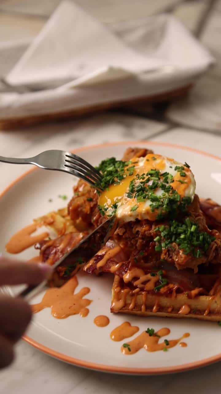 Tagliare un delizioso piatto di pollo e waffle con un uovo fritto dal tuorlo morbido