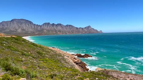 Koeel-Bay-Dappat-Se-Gat-Filmische-Windige-Brandungswellen-Krachen-Atemberaubender-Kogel-Bay-Strand-Kapstadt-Südafrika-Küstenlinie-Aqua-Tiefblaues-Wasser-Gordon&#39;s-Bay-Garden-Route-Nach-Vorne-Schwenk-Nach-Links