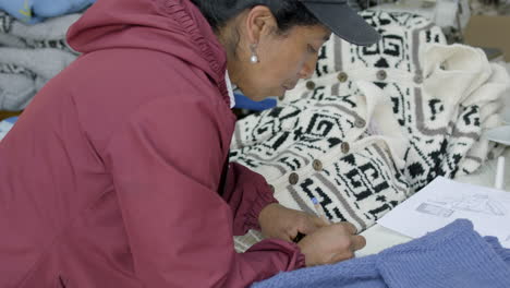 Indigenous-woman-writing-on-paper,-surrounded-by-wool-thread-clothing