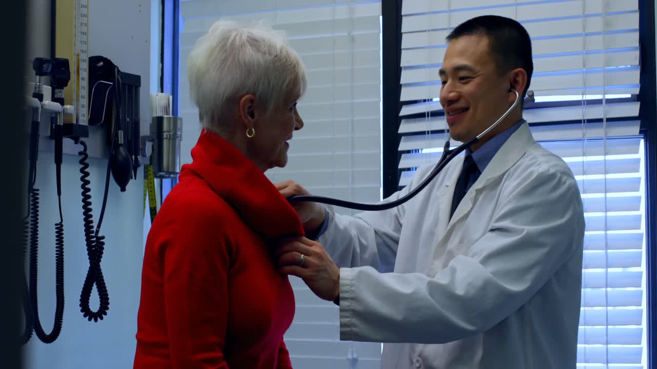 Side view of young Asian male doctor examining a senior patient in the clinic 4k