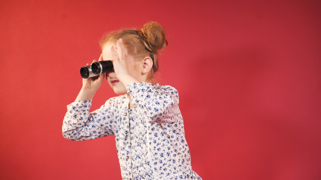 Bambina che guarda attraverso un binocolo. Isolata su sfondo rosso