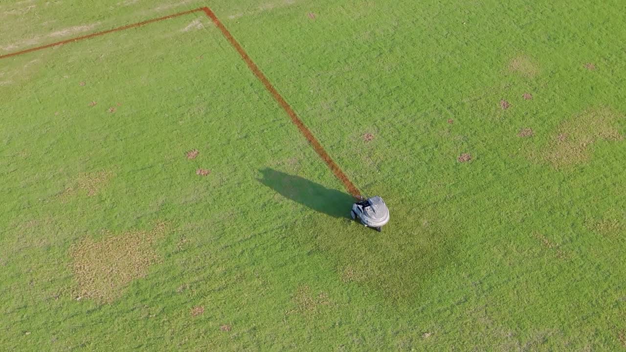日中に、自動機械が芝生の競技場に正確に赤い線を引く