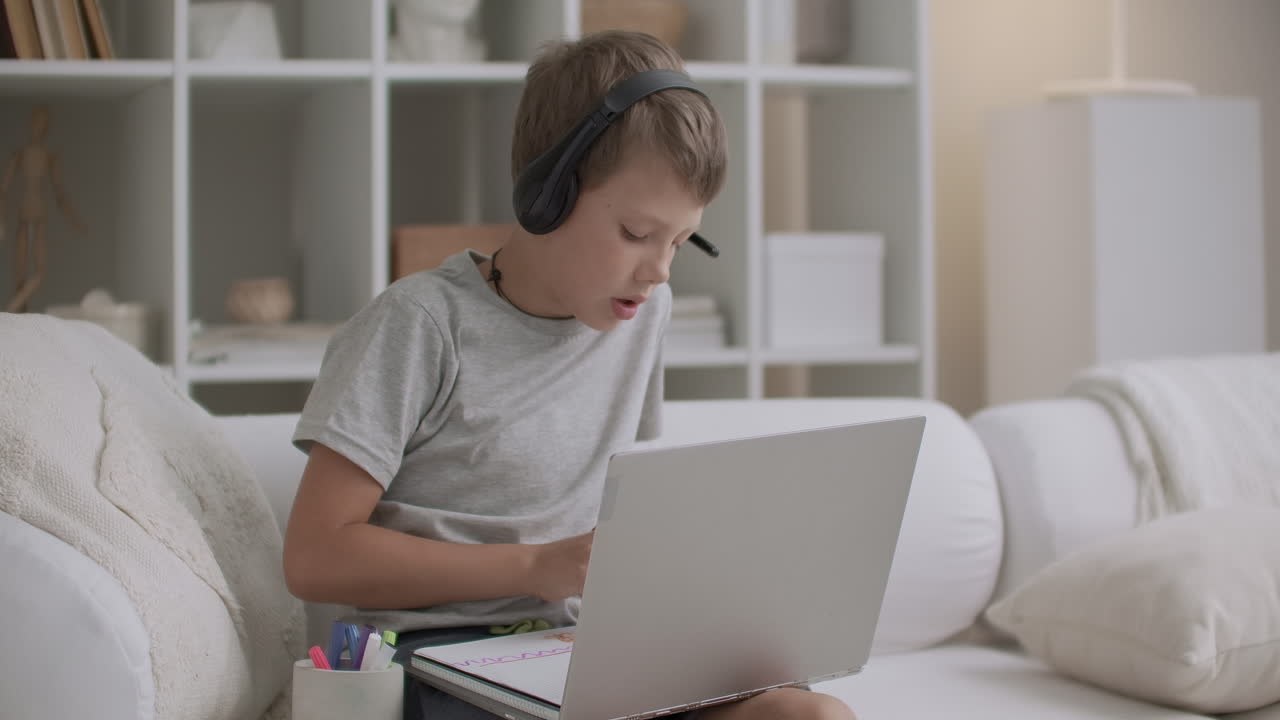 мальчик с наушниками на голове и ноутбуком на столе рисует дома в период изоляции в период пандемии коронавируса