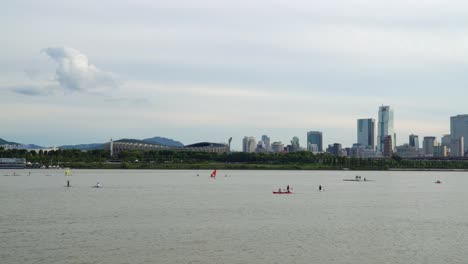 Windsurfen-Und-Kajakfahren-Am-Fluss-Han-Mit-Olympiastadion-Und-Handelsturm-Im-Hintergrund-In-Seoul,-Südkorea