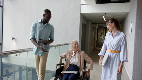 discussing work, business colleagues with woman in wheelchair holding tablet in hallway