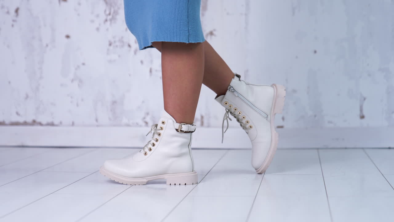 Unrecognized woman in blue dress shows the light leather boots with laces. New fashionable stylish footwear at white backdrop.