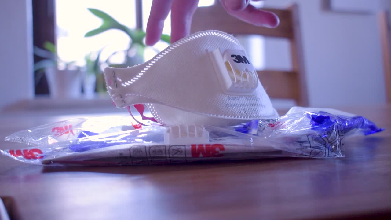 A hand interacting with a 3M respirator mask and its packaging