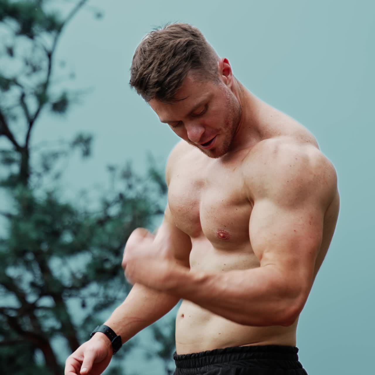 Muscular Caucasian man with naked torso showing his strong muscles. Sportive guy exercising outdoors