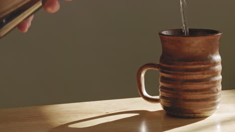 close up shot of person pouring freshwater into mug on table at home during sunny day