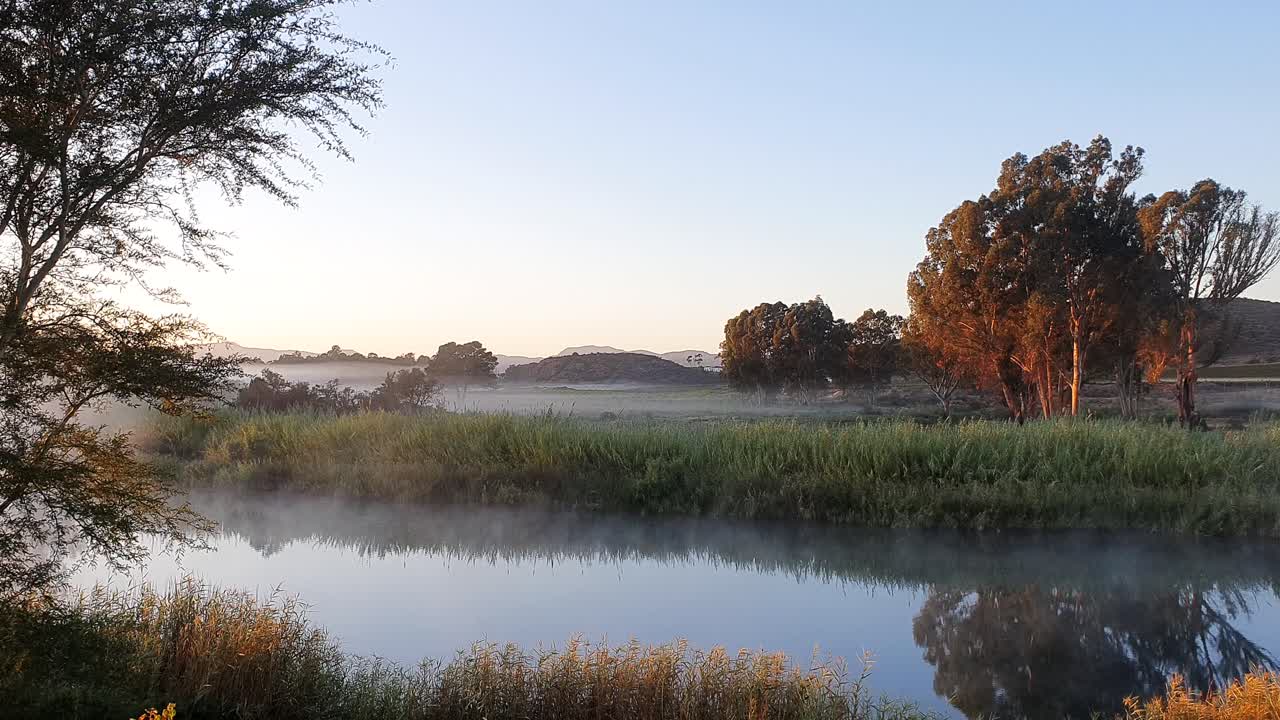 Early morning mist swirls over a calm and slow flowing river in South Africa