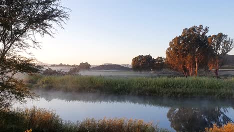 early morning mist swirls over a calm and slow flowing river in south africa