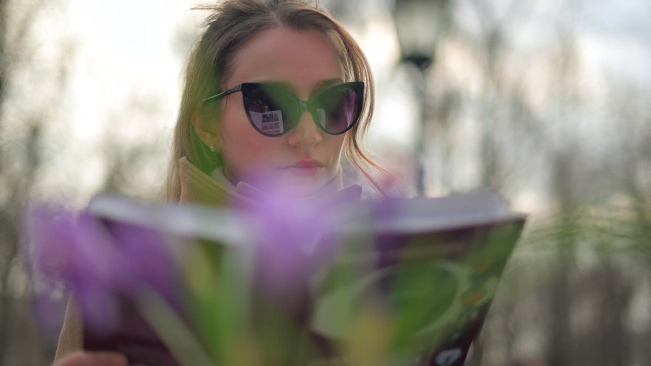 Brunette woman in brown coat reading a book at a terrace