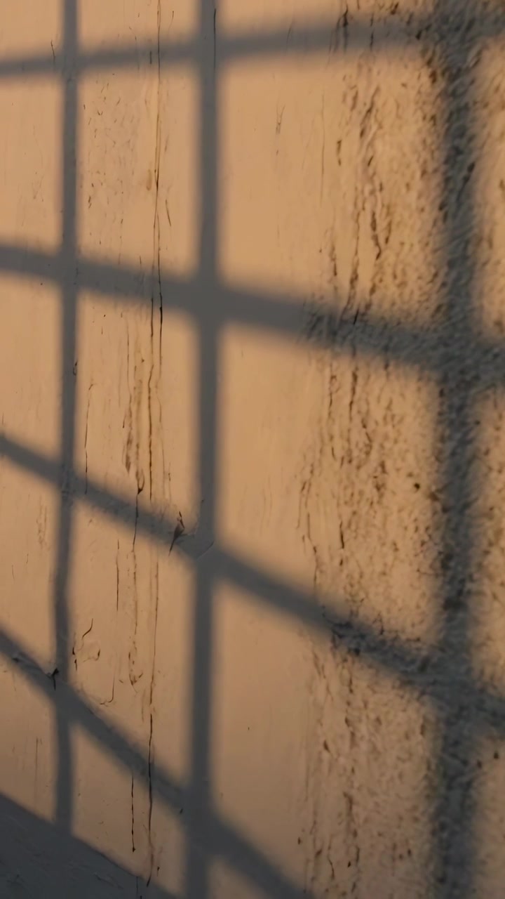 Vertical video: Sliding grid shadow moving across stained wall in room sun drifting showing streaks