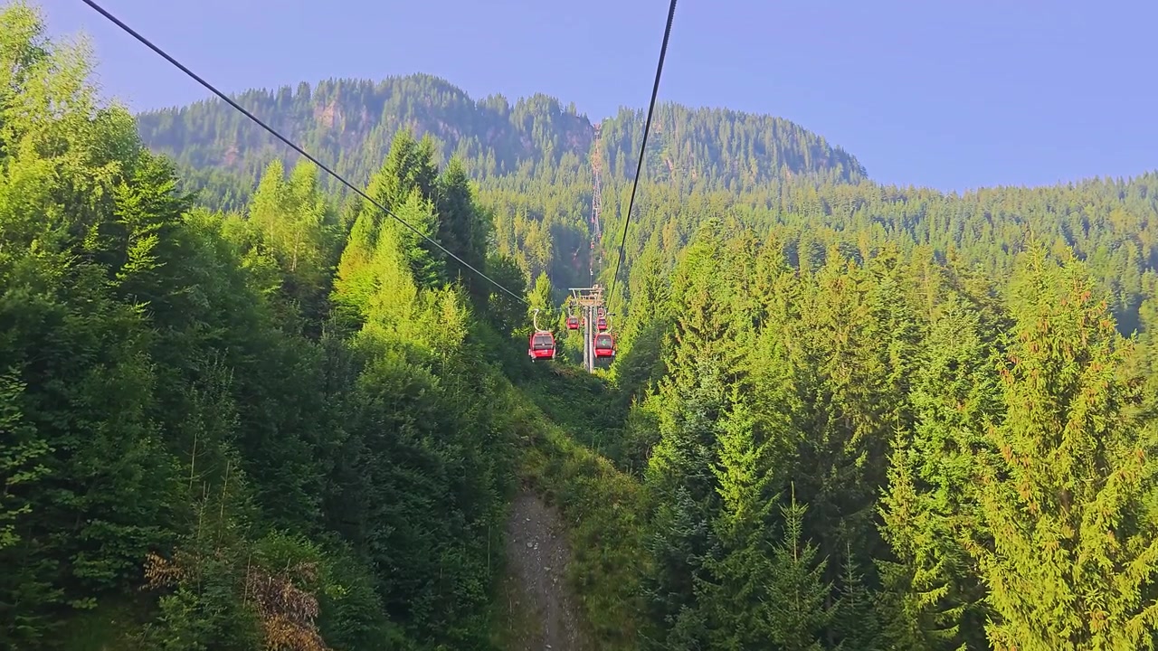 Splendida vista da una gondola a Kitzbühel, Austria, che mostra funivie rosse, tetti di villaggi alpini, prati verdi, foreste sempreverdi e montagne tirolesi sotto la luce solare estiva