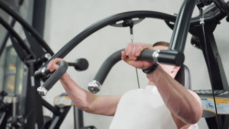 fitness enthusiast working out on chest press machine hands gripping curved handle eyes closed face showing tension muscles contracting under gym lighting on steel equipment rubber floor