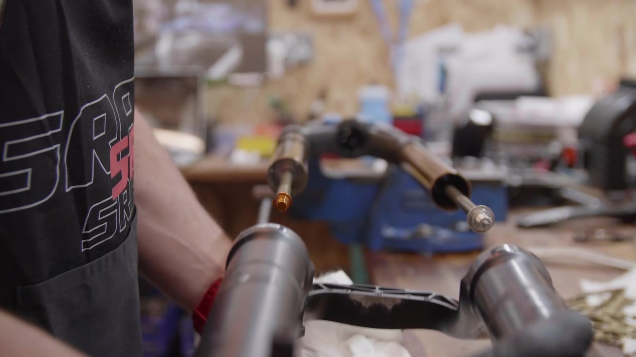 Mountain bike workshop. Male, professional mechanic maintaining bike forks. Forks in a vice. Close up of hands wearing rubber gloves pulling forks apart.