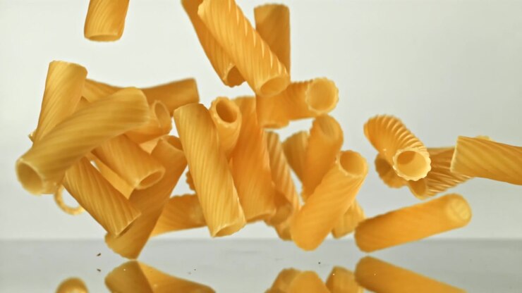 Tubetti di pasta secca che cadono al rallentatore su sfondo bianco