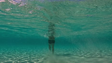 underwater back view in shallow water of man walking on seabed raising clouds of sand floating in turquoise tropical sea