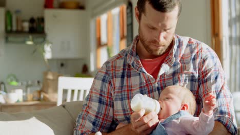 Front-view-of-mid-adult-caucasian-father-feeding-milk-his-baby-from-bottle-in-a-comfortable-home-4k